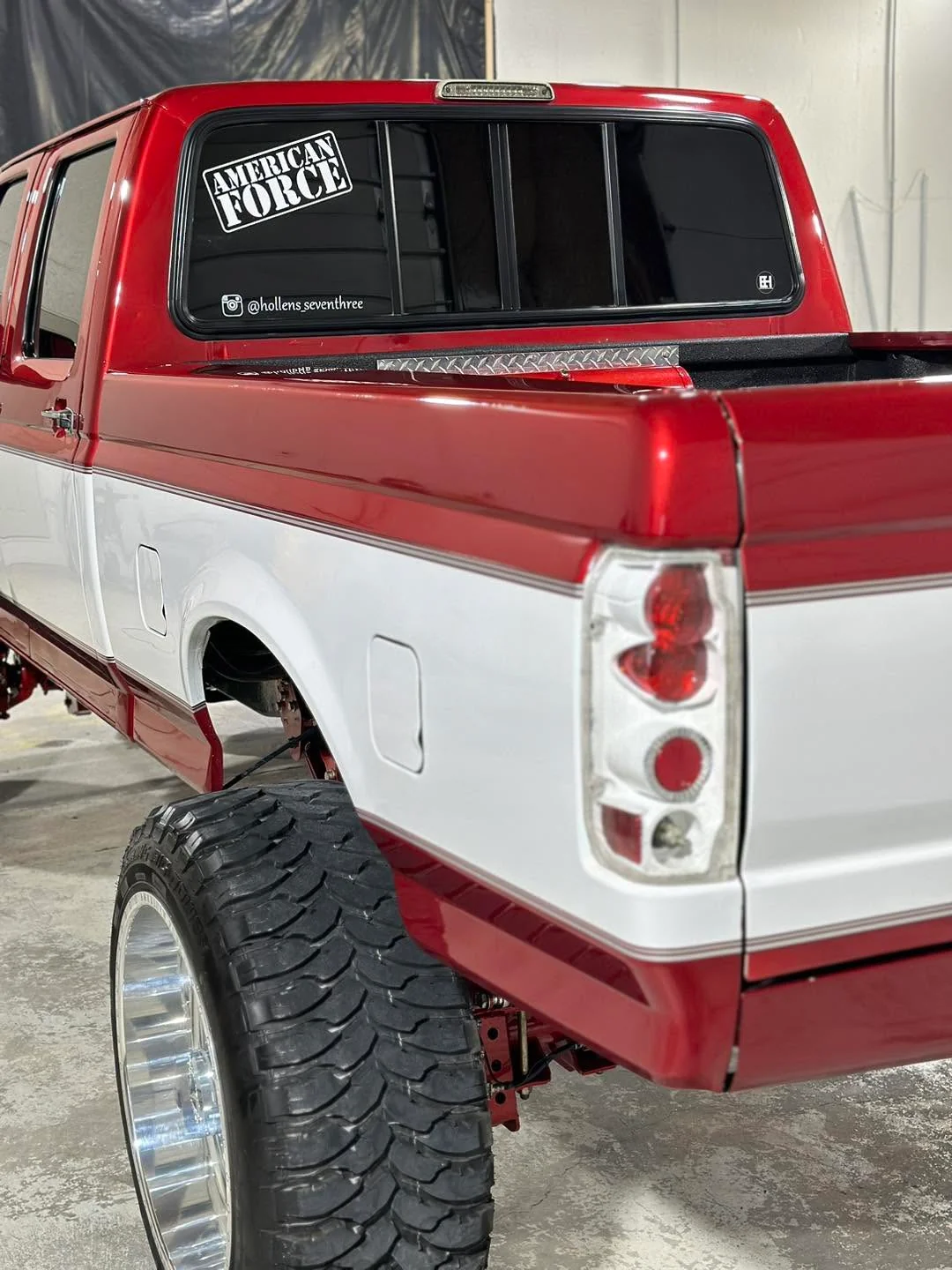 Red and white lifted Ford crew cab pickup, rear three-quarter view