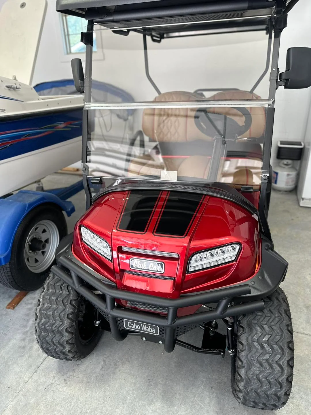 Red Club Car lifted golf cart, front view beside boat