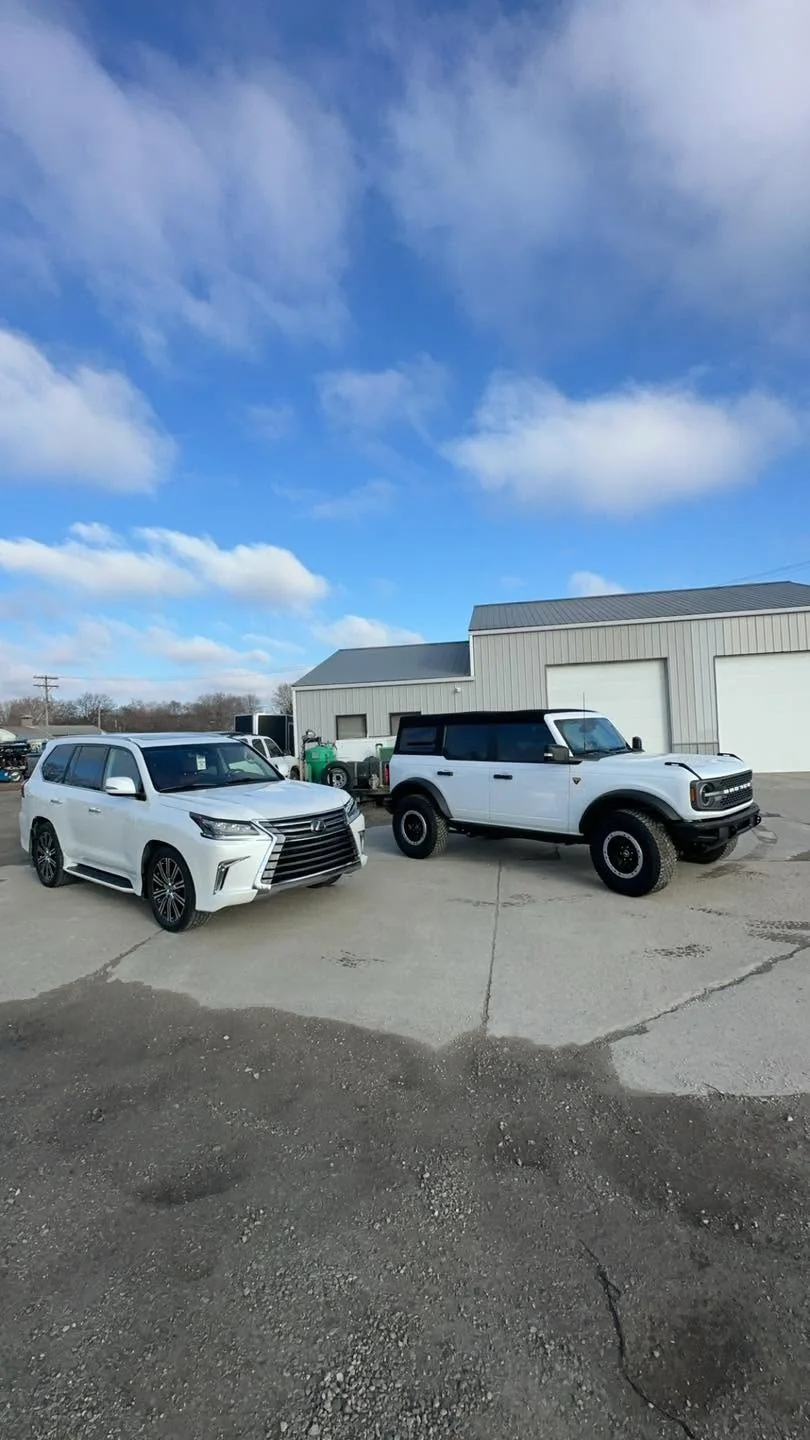 White Lexus LX SUV and white Ford Bronco parked outside