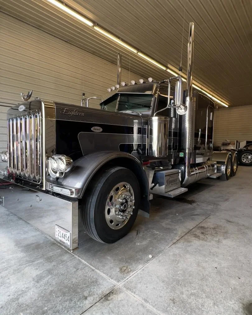 Dark Peterbilt semi-truck cab, front three-quarter view in shop